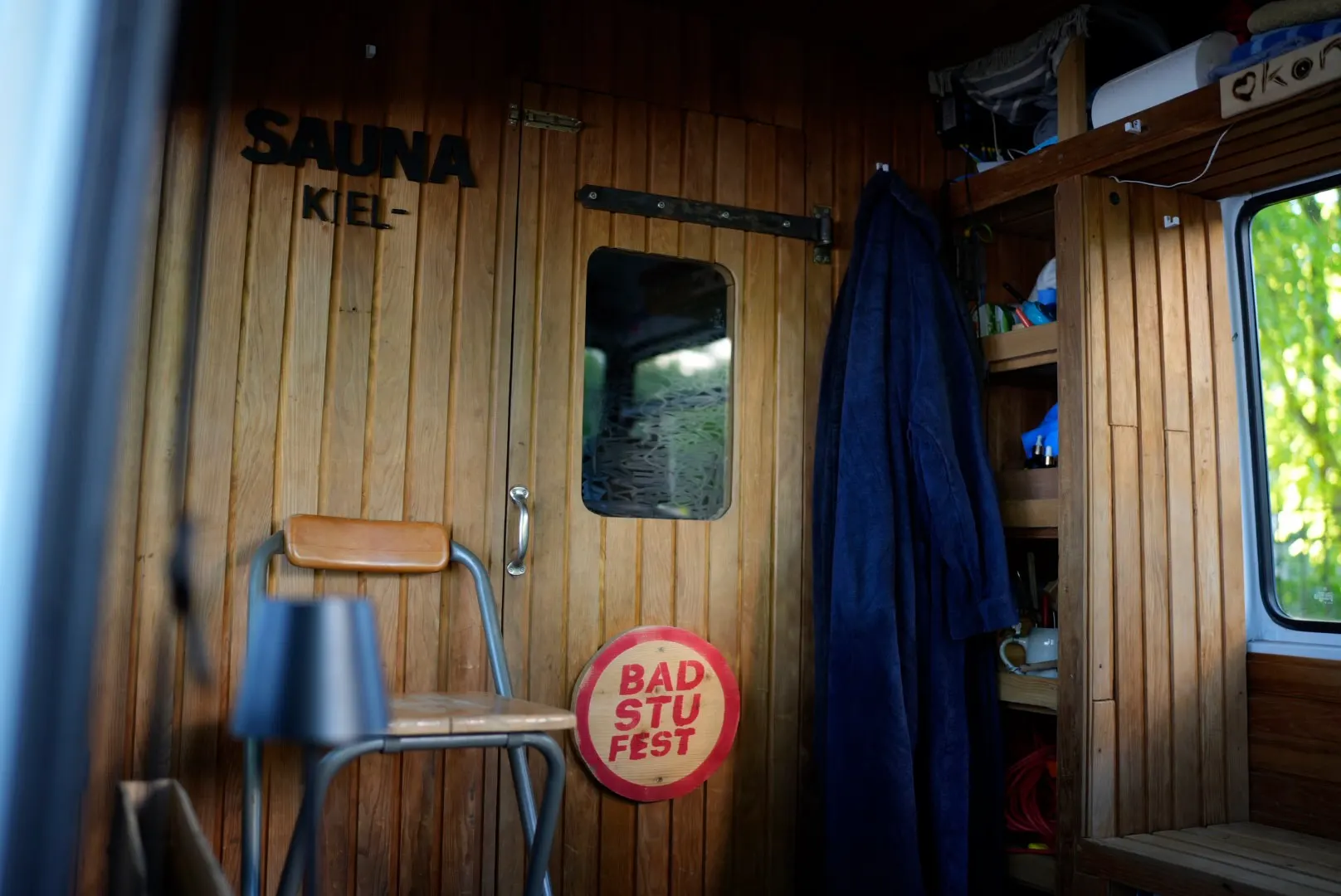 Blick in den Bus: eine Holzwand mit dem Schriftzug SAUNA KIEL, ein Bademantel hängt an der Tür, daneben ein Stuhl.